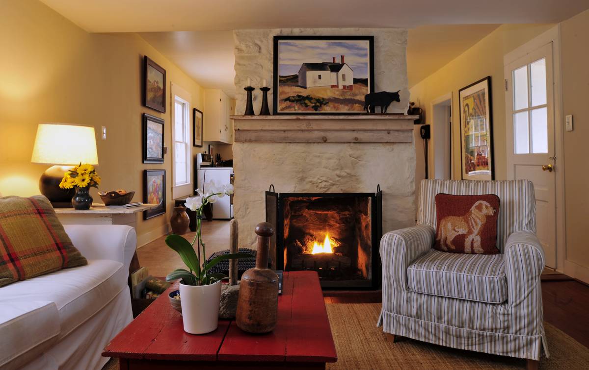 A farmhouse has rural decor, like a fireplace, painting of a farmhouse, bull statue, and red coffee table.
