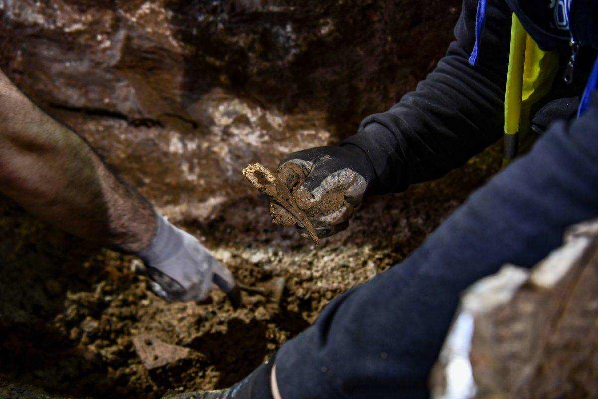 An archaeologist picks up an artifact from a burial ground as another archaeologist points at another.