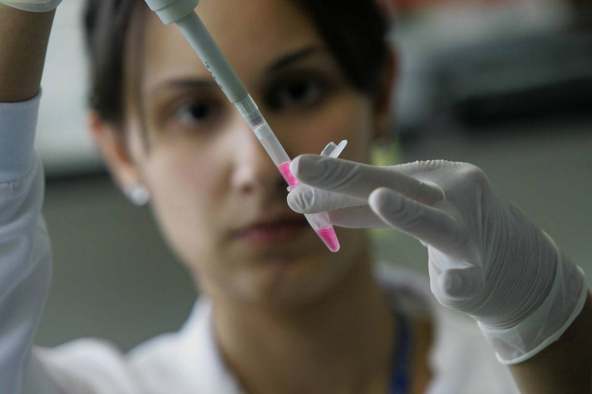 A woman holds up a dropper filled with dna samples to study.