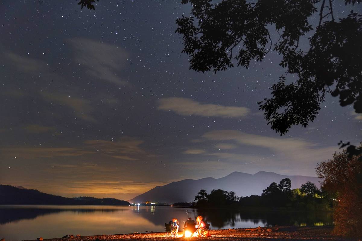 People by a campfire under the stars at Derwent Water near Keswick in the Lake District