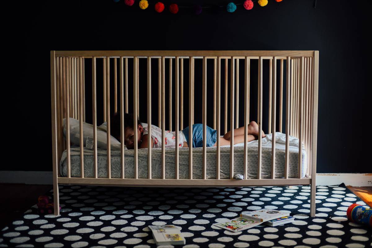 Baby in navy blue nursery laying in crib with polka dot area rug