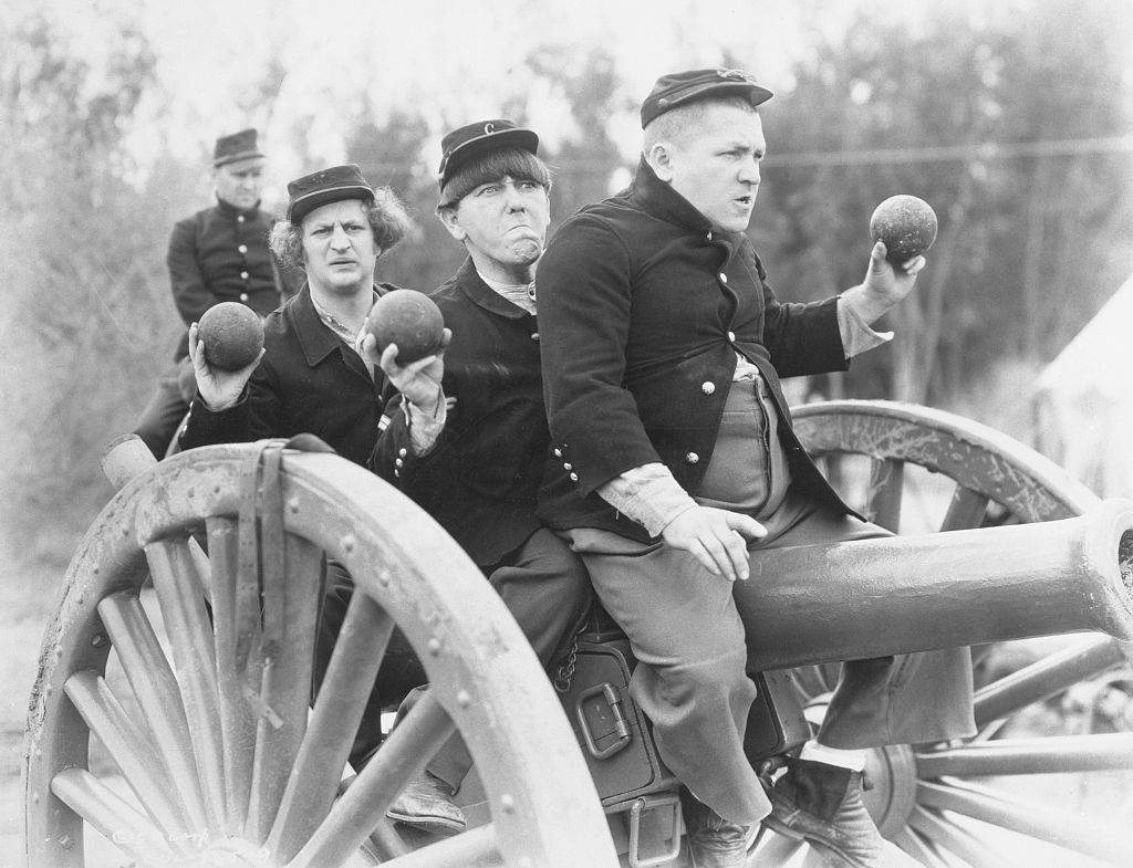 Three Stooges actors filming while seated on rolling canon