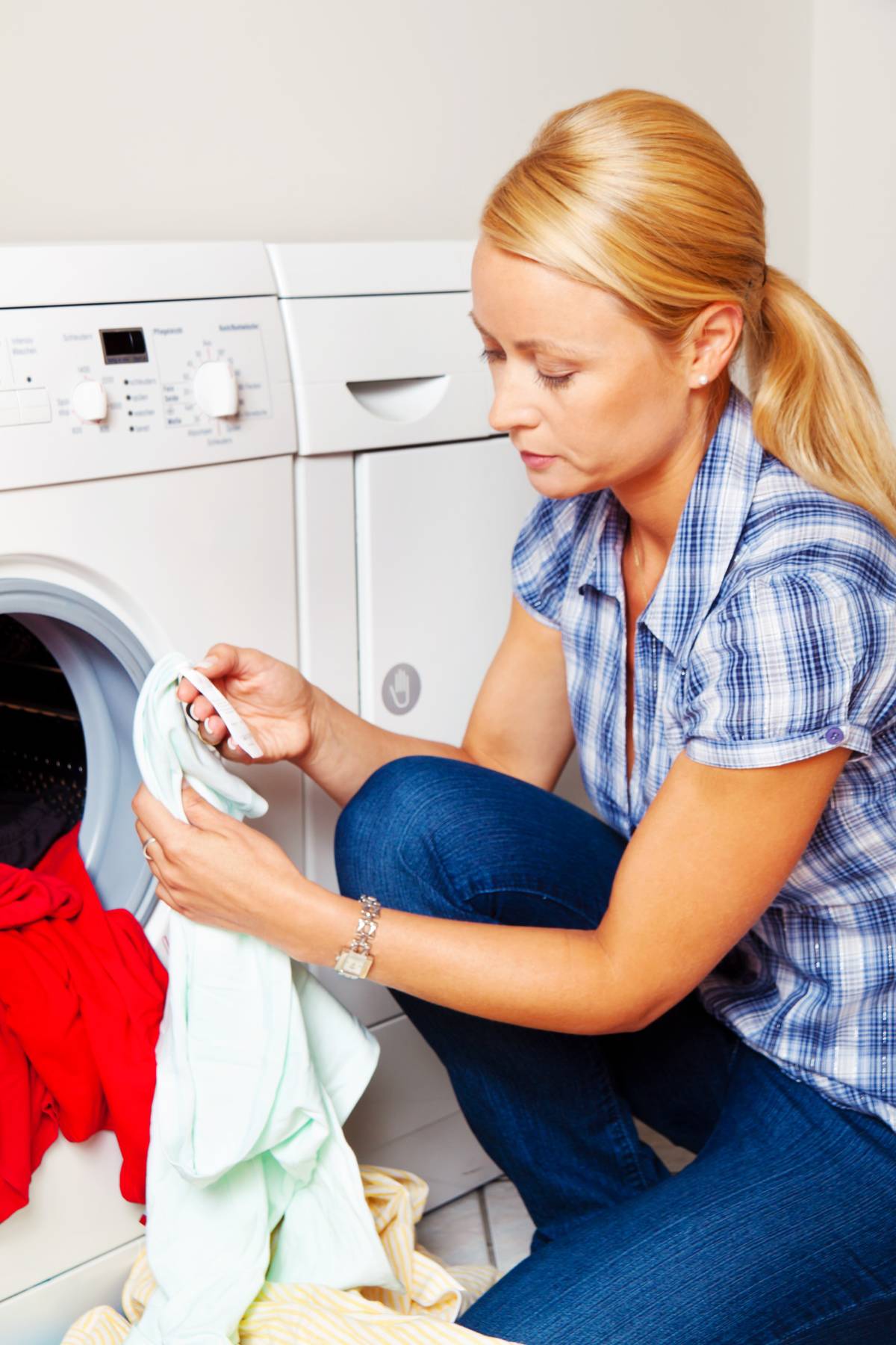 Blonde woman checking laundry as she pulls it out of dryer