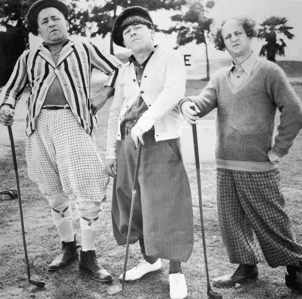 circa 1938: The Three Stooges, dressed in golfing attire, posing with golf clubs on a golf course. Left to right: Curly Howard Moe Howard  and Larry Fine