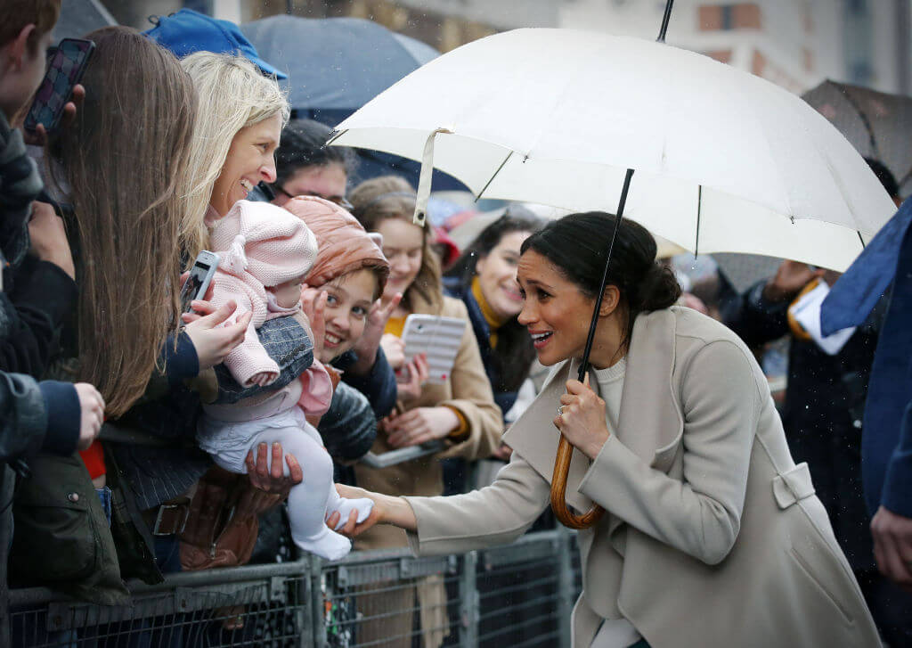 Meghan Markle greets a baby of the public holding a white umbrella