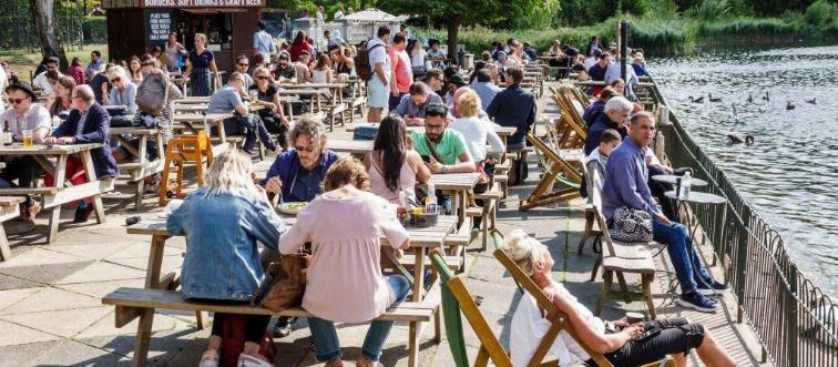 People sunbathe near waters edge on picnic tables 