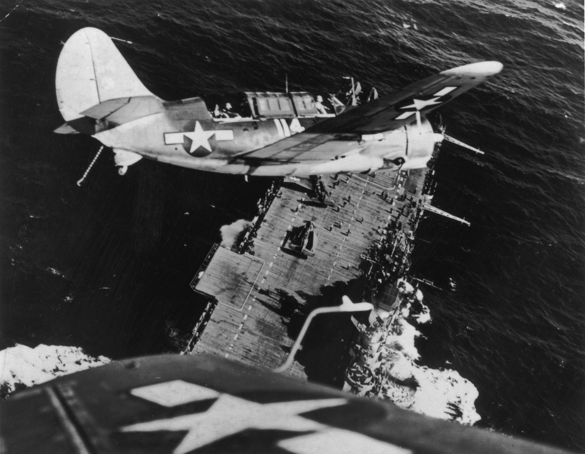 A US Navy Curtiss Helldiver (SB2C) prepares for a landing on an aircraft carrier after a mission against a Japanese warship.