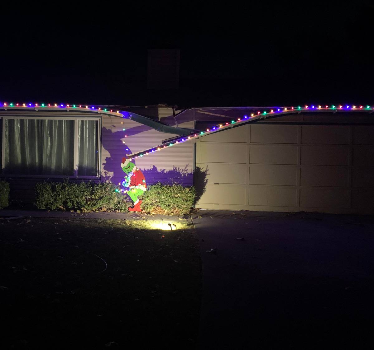 House with damaged roof and Christmas lights draping down to Grinch decoration