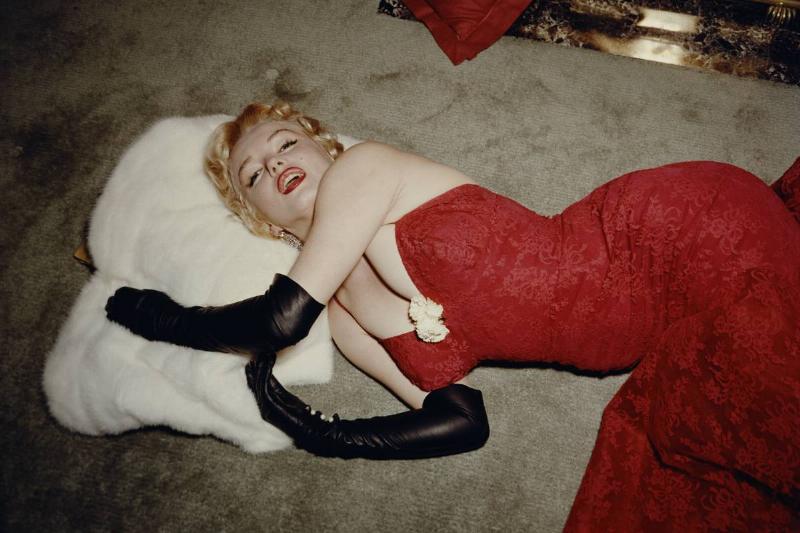 1955:  EXCLUSIVE American actor Marilyn Monroe (1926  - 1962), wearing a  red brocade evening gown and long black gloves, lying on a carpet and 
using a white fur stole as a pillow.