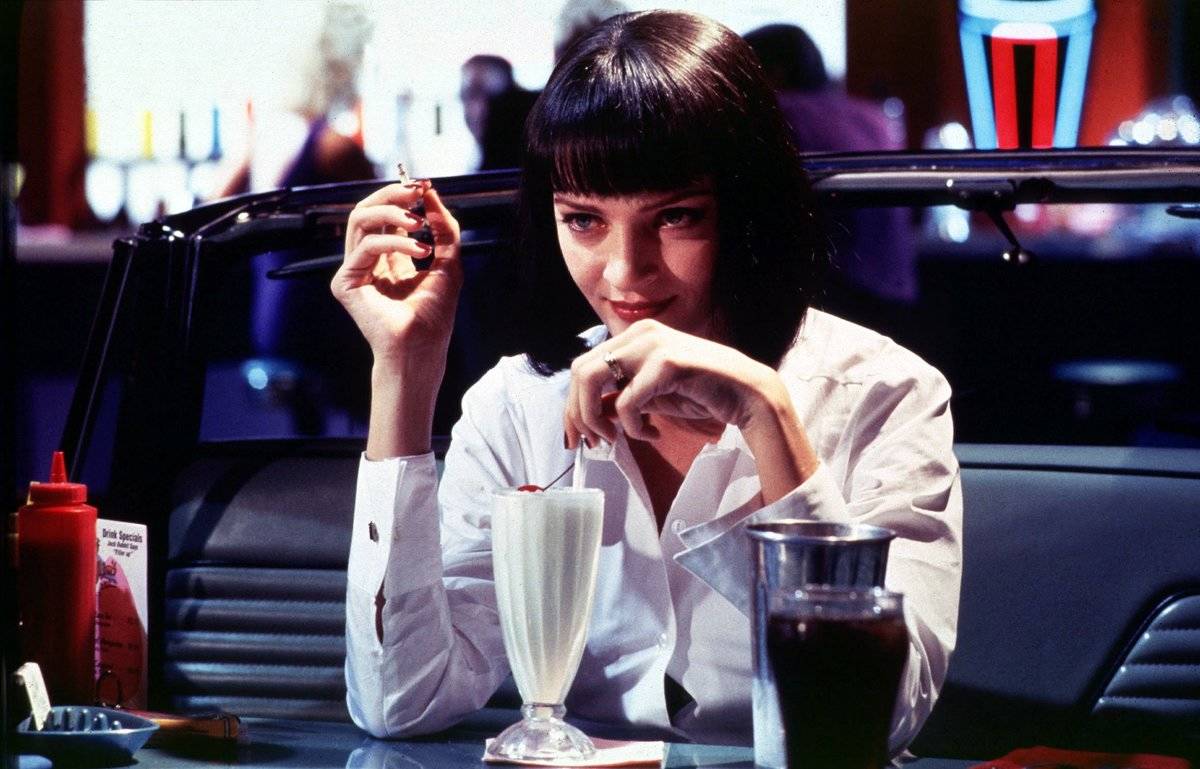 Uma Thurman sitting at 50s diner booth with milkshake as Mia Wallace in Pulp Fiction