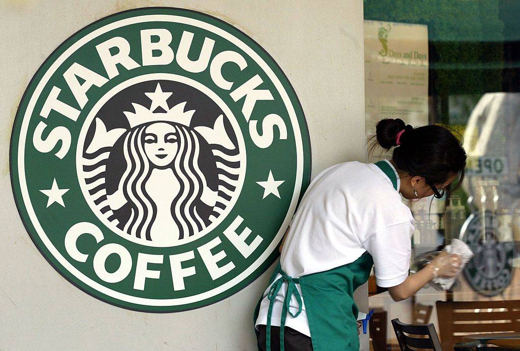 A Starbucks worker cleans the window next to a company logo at a coffee store