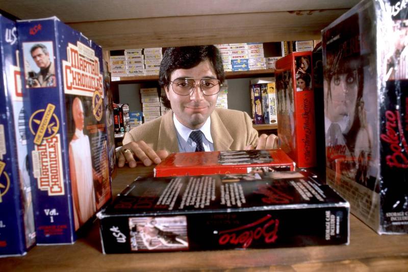 Video store owner Jimmy Russo poses for a portrait behind a bookshelf  with VHS tapes circa September, 1985 in Los Angeles, California.