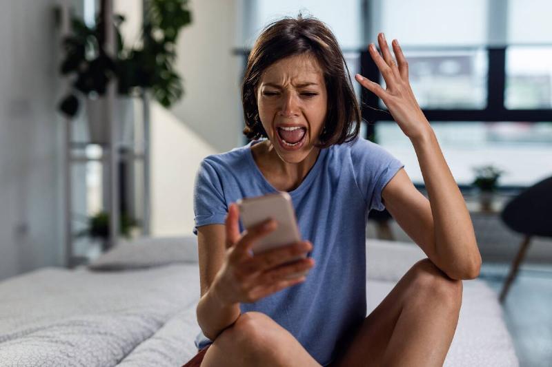 woman yelling at phone while sitting on bed