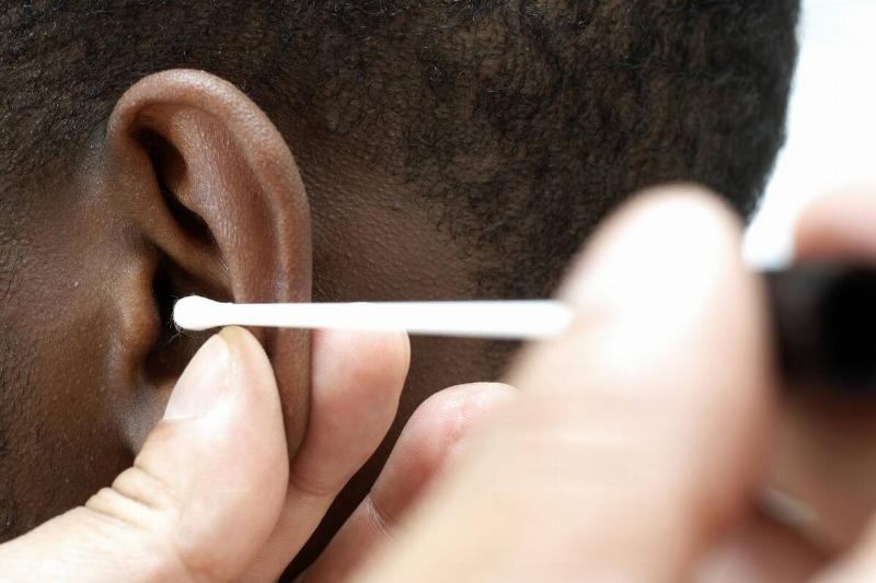 GP using cotton bud to clean ear canal of young male patient