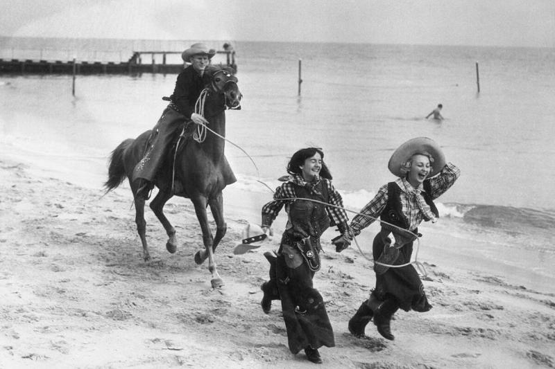 Cowboy on horse catching laughing women on beach