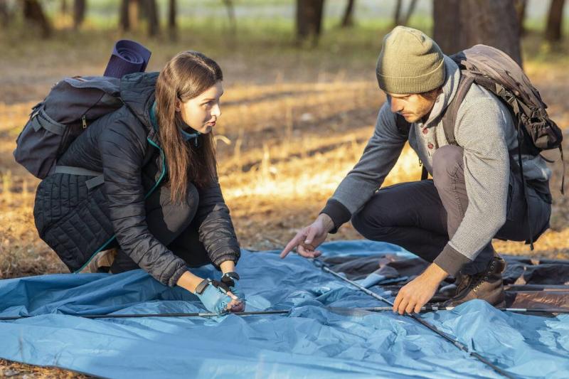 Couple of hikers pitching the tent before a sunset in a forest.