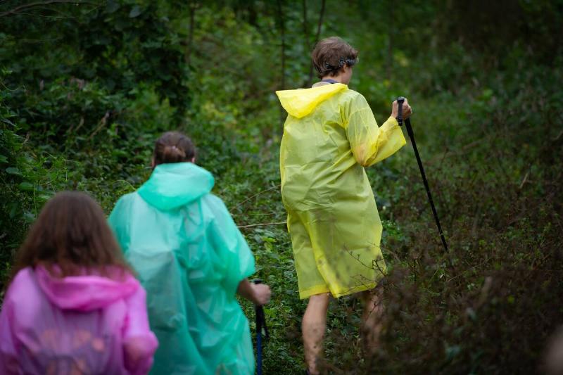 Group of friends in raincoats walking on the forest path.
