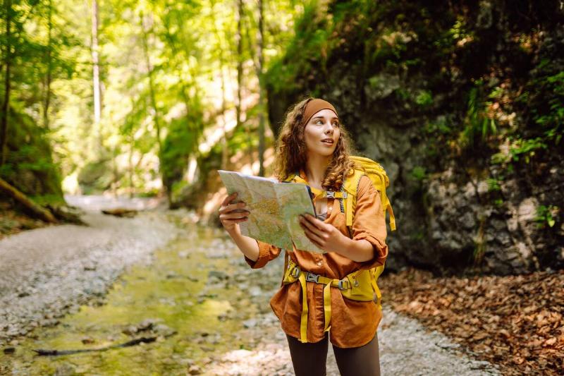 Young woman on a mountain path with a map in her hands, exploring hiking trails.