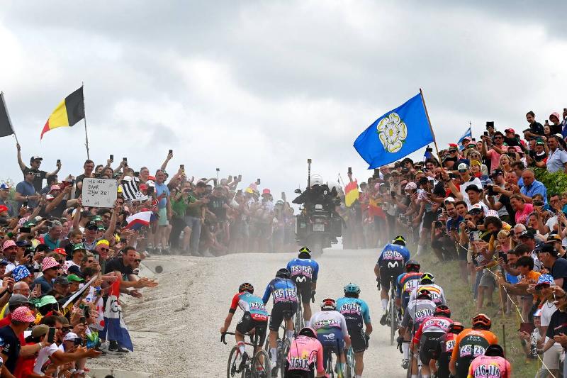 A general view of the peloton passing through a gravel strokes sector while fans cheer during the 111th Tour de France 2024, Stage 9.