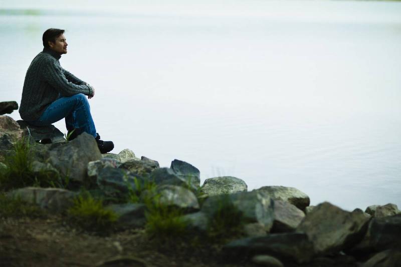 Man sitting on rocks and looking at water.