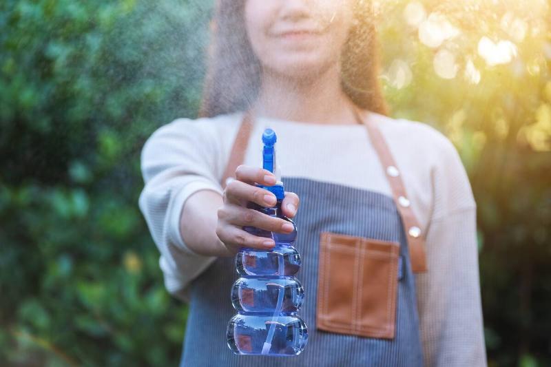 A woman with apron watering plant by foggy spray in garden.