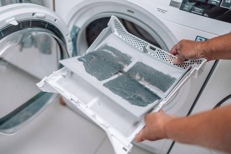 female hand taking the lint out from dirty air filter of the dyer machine.