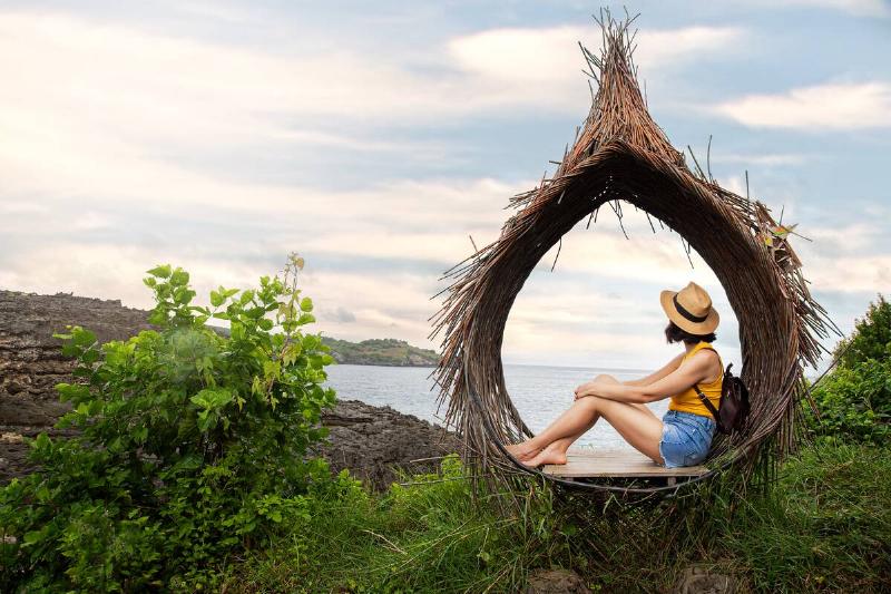 Young female traveler relaxing sitting in straw nest looking at ocean view.
