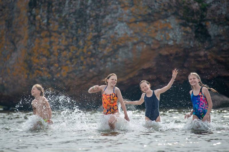 Four little girls are running on water on a summer sea beach and having fun.