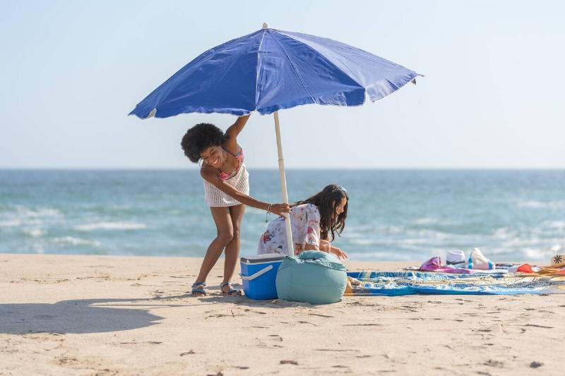 Friends laughing and opening the umbrella, on the shore of the beach.