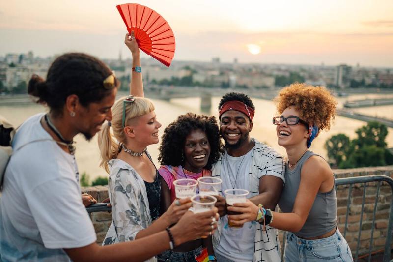 Friends are toasting with beer while enjoying a summer music festival at sunset.