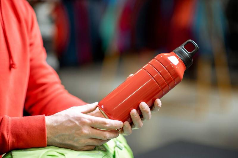 Man holding red thermos for hiking.