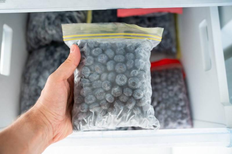 Man hands hold zip bag with blueberries, putting into freezer.
