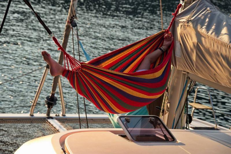 Man relaxing in the hammock set on the sail boat anchored in the sea.