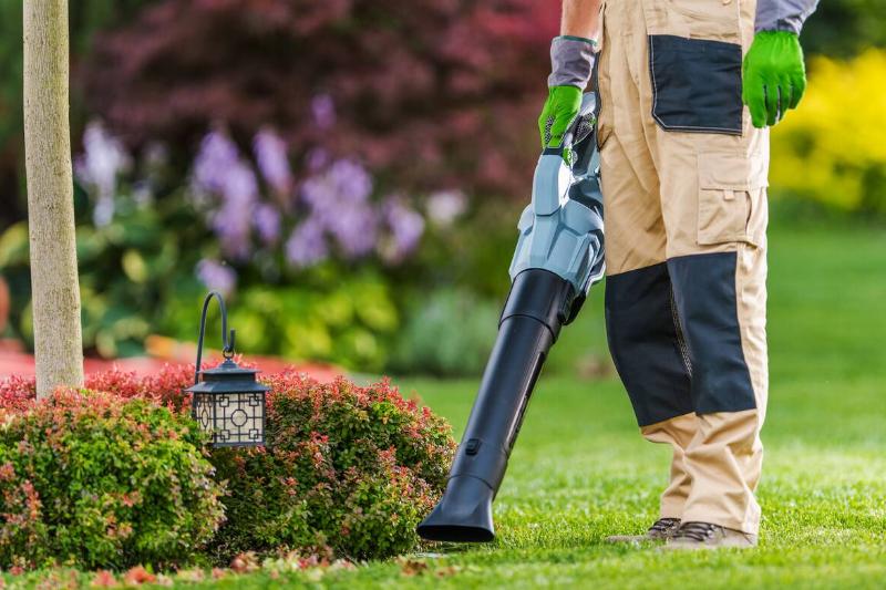 A person in gardening attire operates a leaf blower.