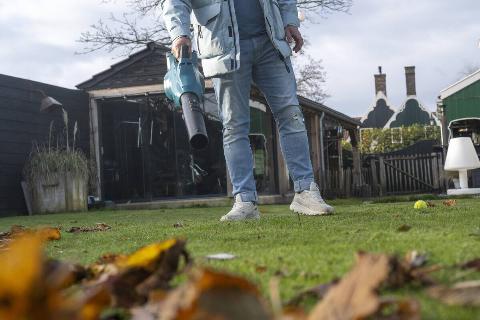 Man using an electric blower to tidy up leaves in the garden of his home.