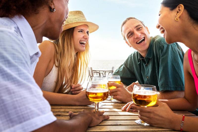 Group of young friends laughing having fun at beach bar drinking beers.