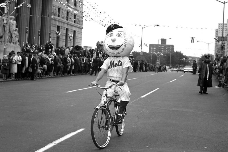 Out of his element, Mr. Met on a bicycle rides in parade on