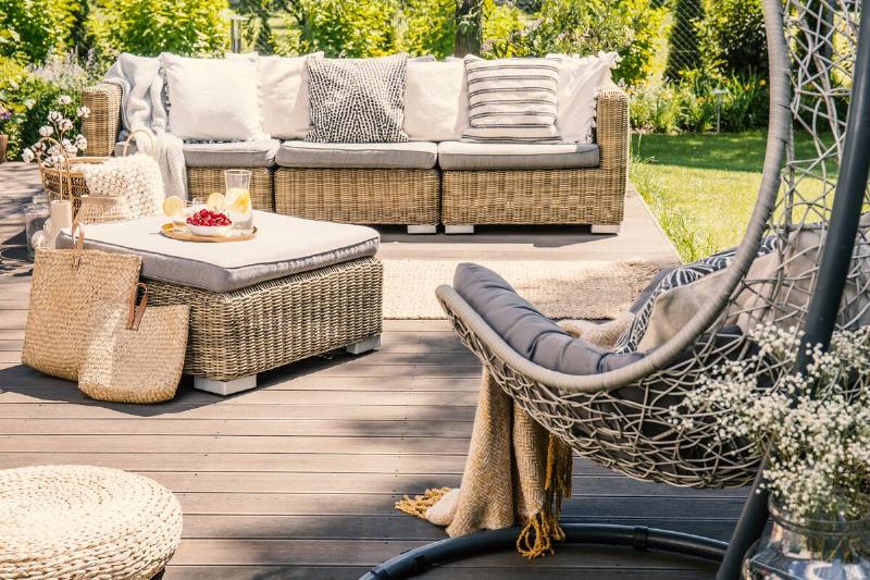 Pillows on rattan couch near table on patio with hanging chair in the garden.