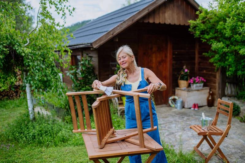 A senior woman cleaning garden furniture with oil. 