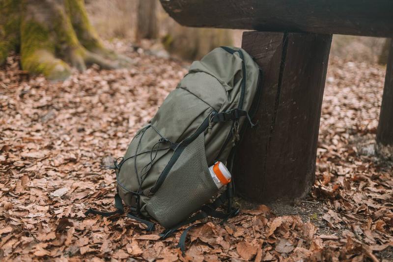 Travel camping backpack or military hunting bag leaning against a tree on the forest floor.