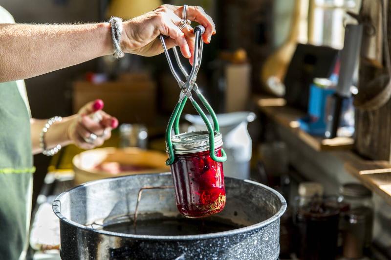 Woman's hands inserting beetroot preserves jar into saucepan for canning. 