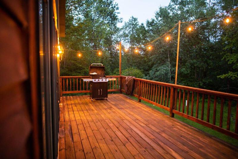 A wooden porch with string lights and grill.