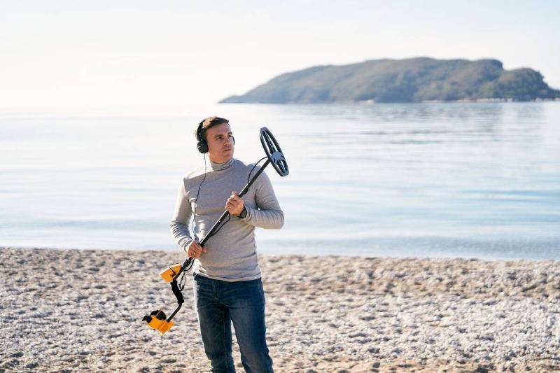 Man holding metal detector on beach.