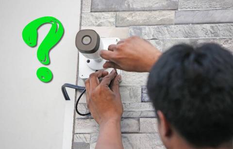 Man plugging in outdoor security camera with question mark