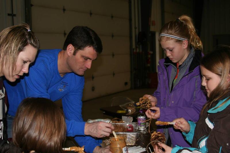 Volunteers showing kids how to put peanut butter and seeds on pinecones for birds.