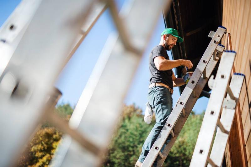 Man painting house on ladder.