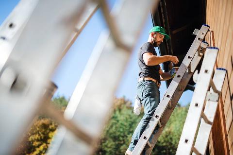 Man painting house on ladder.
