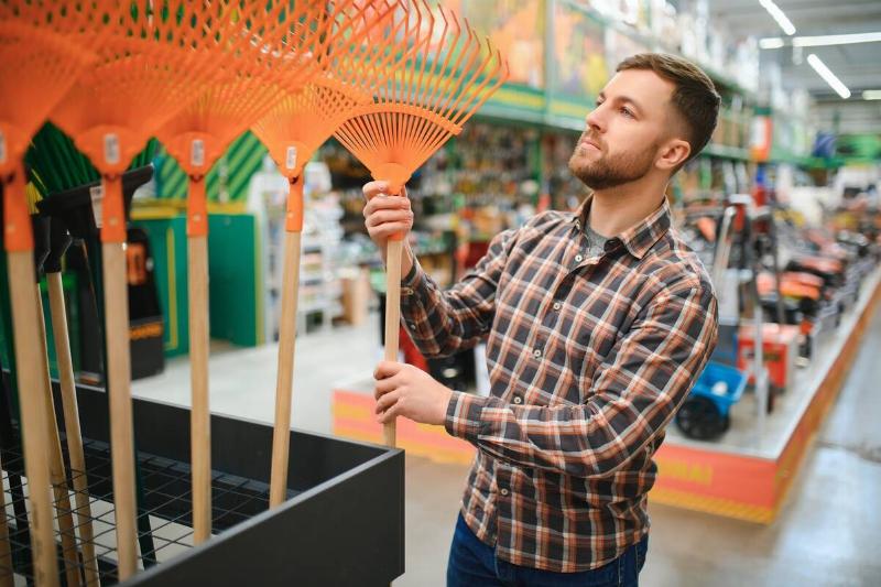 A young man buying a rake in a gardening equipment store.