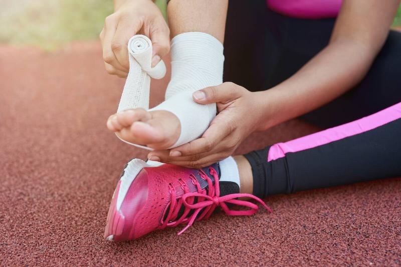 Close up of female child sitting on asphalt and bandaging injured leg