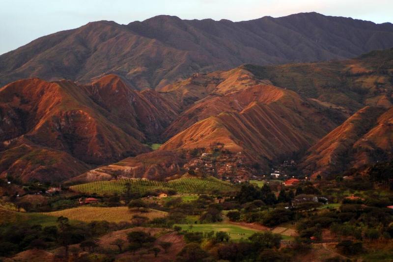 Brown mountains with trees in the foreground and a village at the feet of the mountains, Vilcabamba, Ecuador.